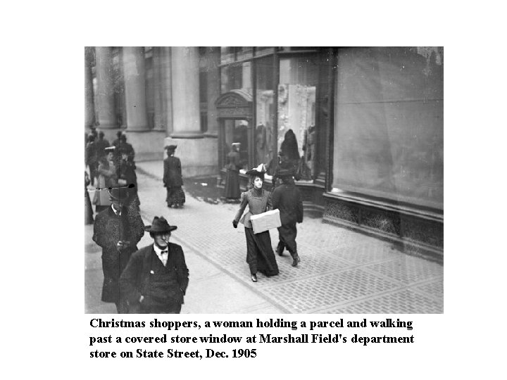 Christmas shoppers, a woman holding a parcel and walking past a covered store window