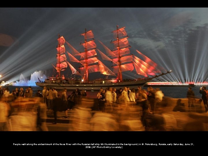 People walk along the embankment of the Neva River with the Russian tall ship