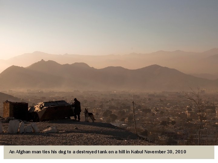 An Afghan man ties his dog to a destroyed tank on a hill in