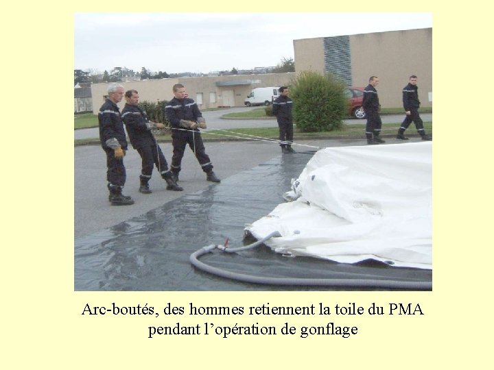 Arc-boutés, des hommes retiennent la toile du PMA pendant l’opération de gonflage 