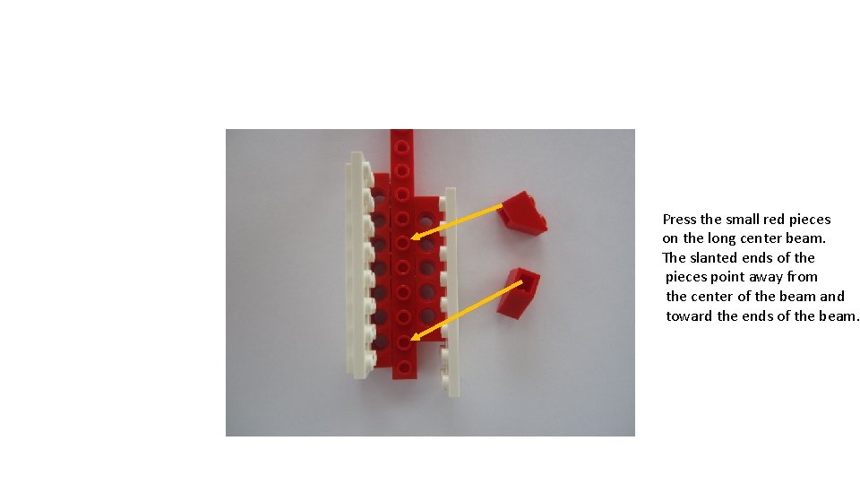 Press the small red pieces on the long center beam. The slanted ends of