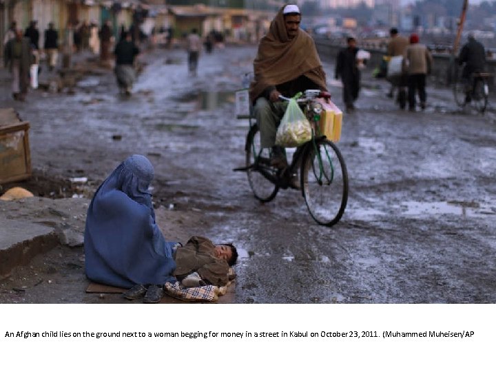 An Afghan child lies on the ground next to a woman begging for money