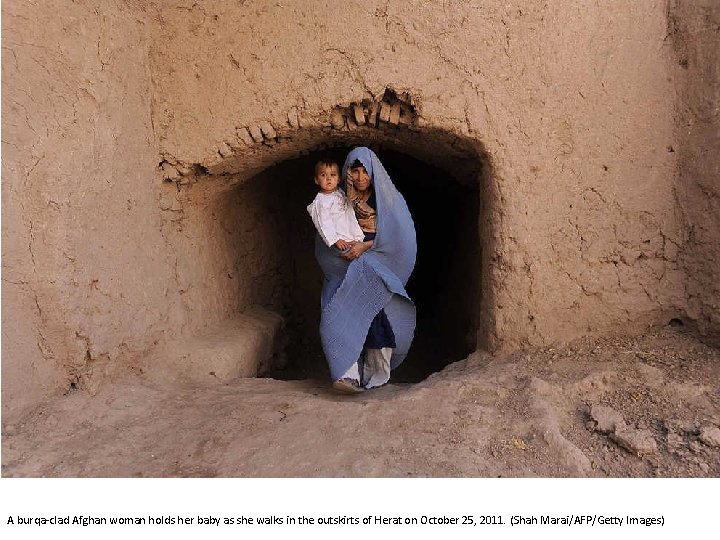 A burqa-clad Afghan woman holds her baby as she walks in the outskirts of