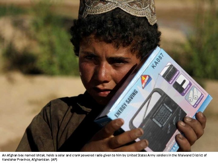 An Afghan boy named Ishtak, holds a solar and crank powered radio given to