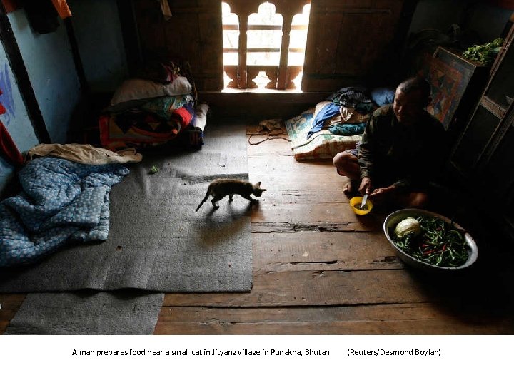 A man prepares food near a small cat in Jityang village in Punakha, Bhutan