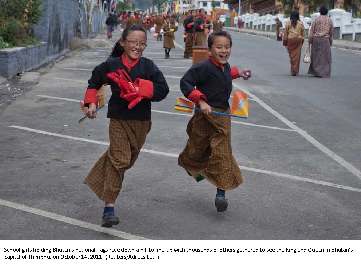 School girls holding Bhutan's national flags race down a hill to line-up with thousands