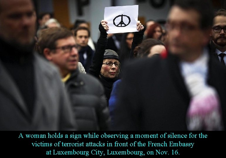 A woman holds a sign while observing a moment of silence for the victims