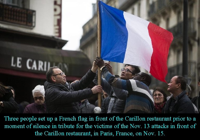 Three people set up a French flag in front of the Carillon restaurant prior
