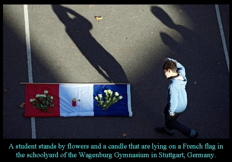 A student stands by flowers and a candle that are lying on a French