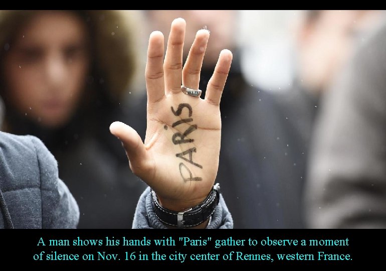A man shows his hands with "Paris" gather to observe a moment of silence