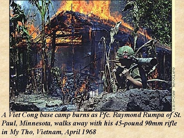 A Viet Cong base camp burns as Pfc. Raymond Rumpa of St. Paul, Minnesota,