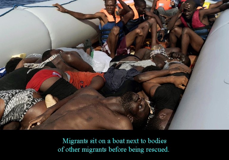 Migrants sit on a boat next to bodies of other migrants before being rescued.