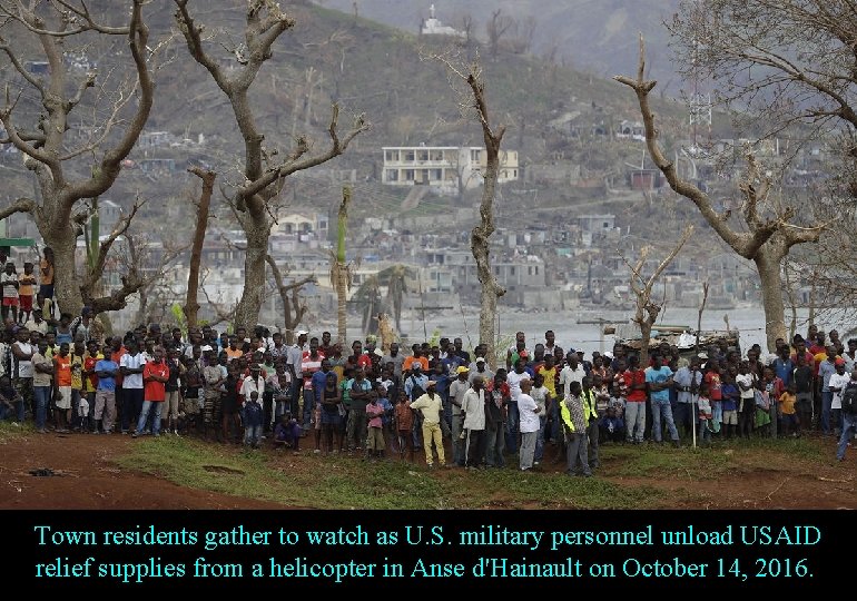 Town residents gather to watch as U. S. military personnel unload USAID relief supplies