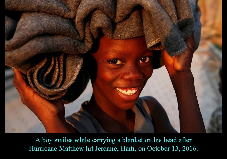 A boy smiles while carrying a blanket on his head after Hurricane Matthew hit