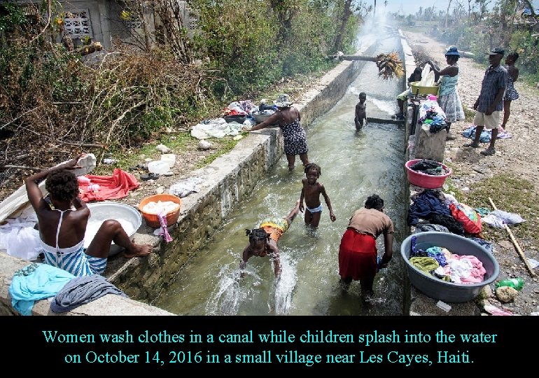 Women wash clothes in a canal while children splash into the water on October