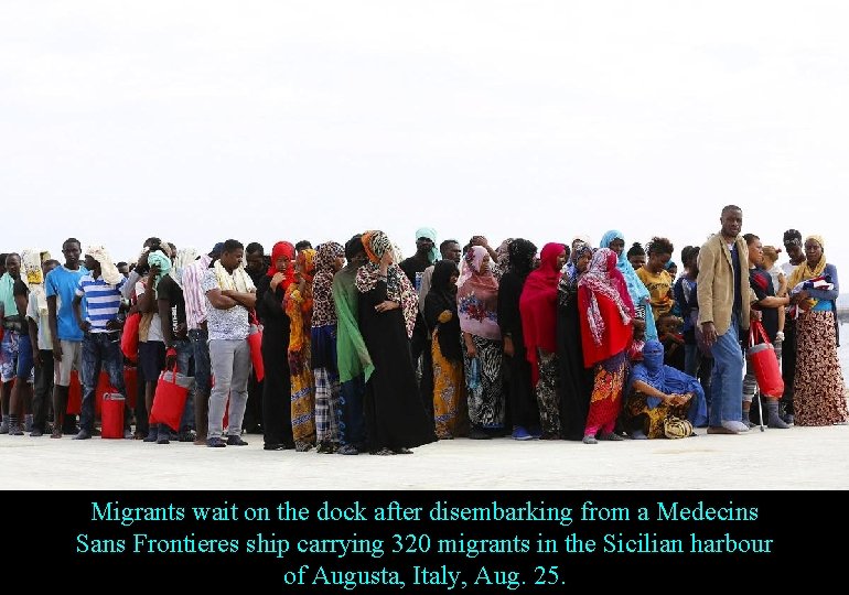 Migrants wait on the dock after disembarking from a Medecins Sans Frontieres ship carrying