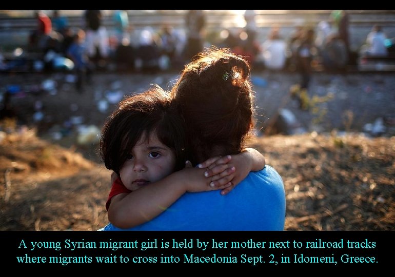 A young Syrian migrant girl is held by her mother next to railroad tracks