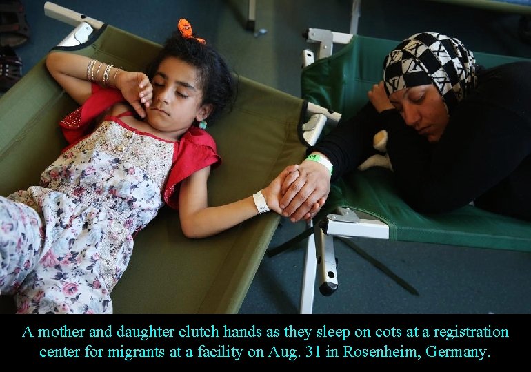 A mother and daughter clutch hands as they sleep on cots at a registration