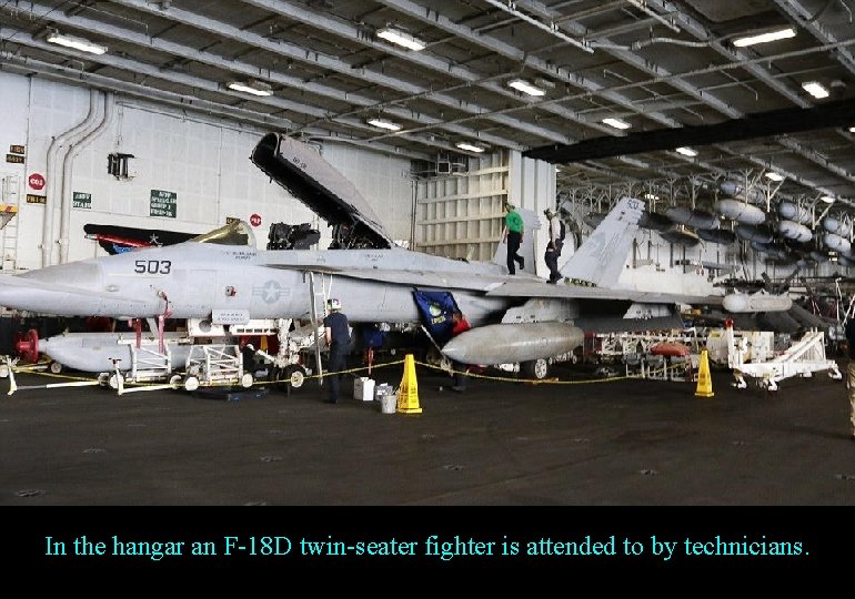 In the hangar an F-18 D twin-seater fighter is attended to by technicians. 