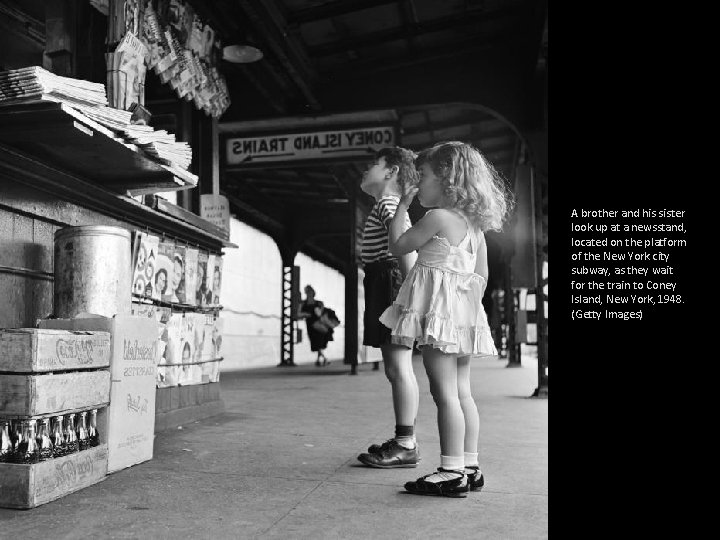 A brother and his sister look up at a newsstand, located on the platform