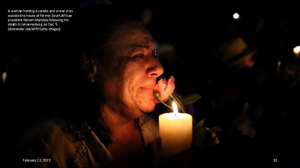 A woman holding a candle and a rose cries outside the house of former