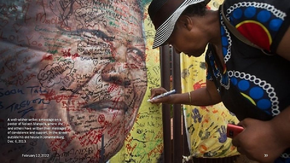 A well-wisher writes a message on a poster of Nelson Mandela, where she and