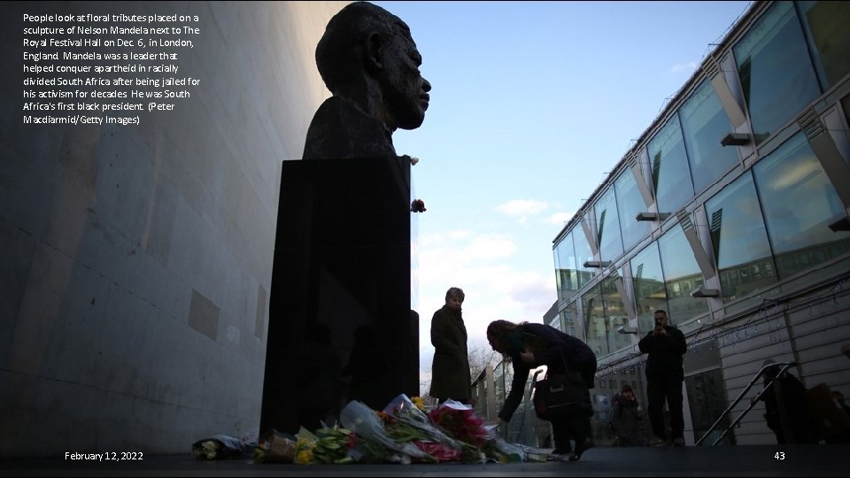 People look at floral tributes placed on a sculpture of Nelson Mandela next to