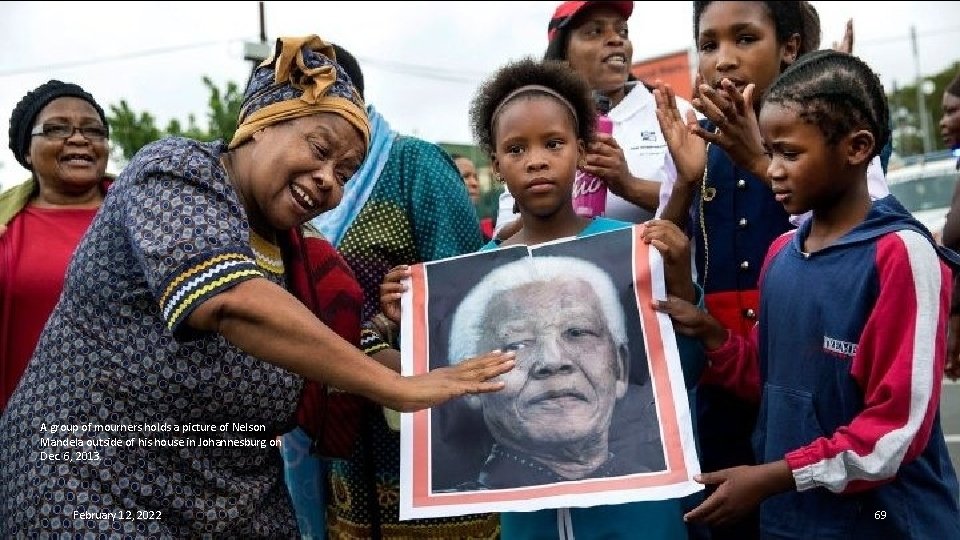 A group of mourners holds a picture of Nelson Mandela outside of his house