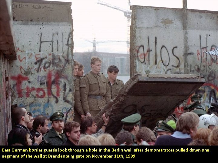 East German border guards look through a hole in the Berlin wall after demonstrators