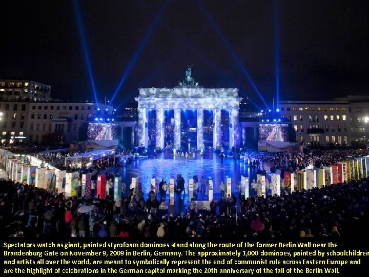 Spectators watch as giant, painted styrofoam dominoes stand along the route of the former