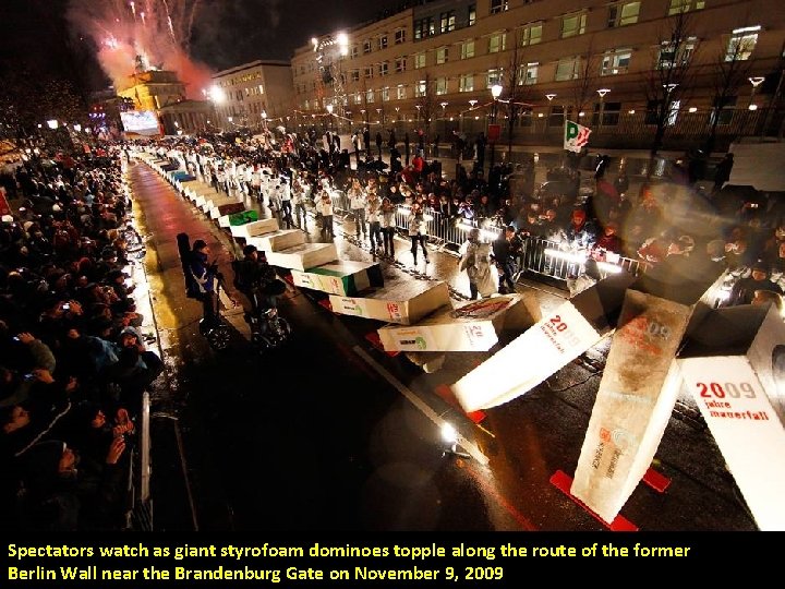 Spectators watch as giant styrofoam dominoes topple along the route of the former Berlin