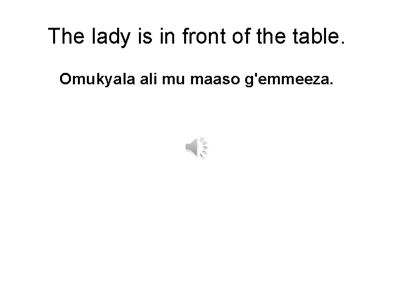 The lady is in front of the table. Omukyala ali mu maaso g'emmeeza. 