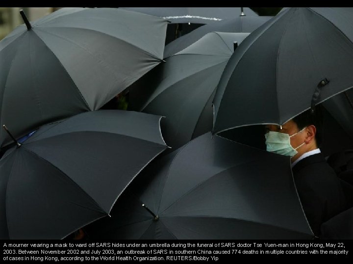 A mourner wearing a mask to ward off SARS hides under an umbrella during