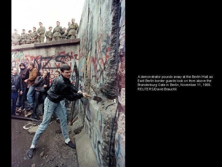 A demonstrator pounds away at the Berlin Wall as East Berlin border guards look
