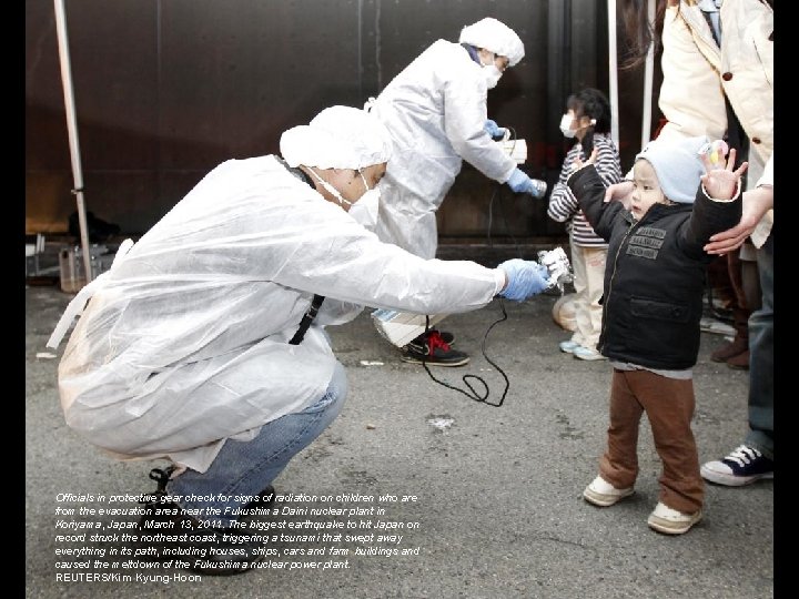 Officials in protective gear check for signs of radiation on children who are from