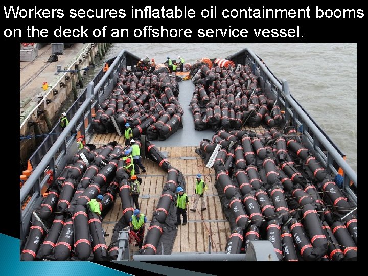 Workers secures inflatable oil containment booms on the deck of an offshore service vessel.