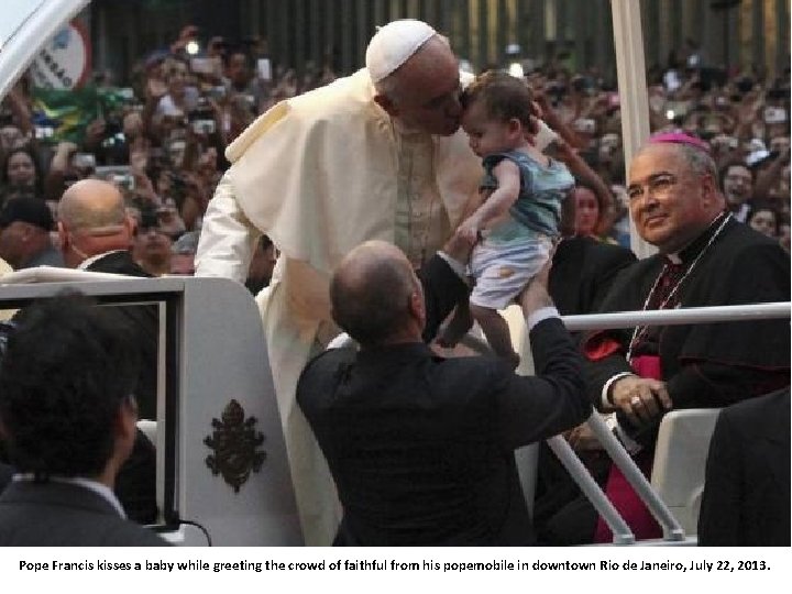 Pope Francis kisses a baby while greeting the crowd of faithful from his popemobile