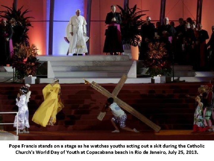 Pope Francis stands on a stage as he watches youths acting out a skit