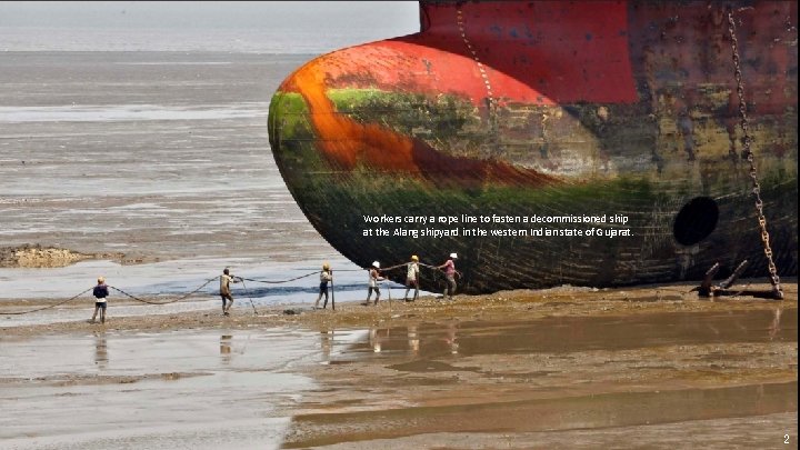 Workers carry a rope line to fasten a decommissioned ship at the Alang shipyard