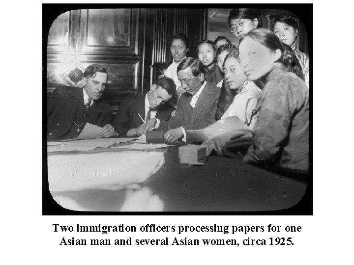  Two immigration officers processing papers for one Asian man and several Asian women,