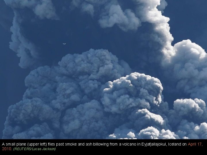 A small plane (upper left) flies past smoke and ash billowing from a volcano