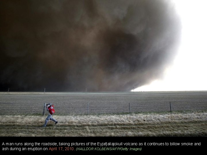 A man runs along the roadside, taking pictures of the Eyjafjallajokull volcano as it
