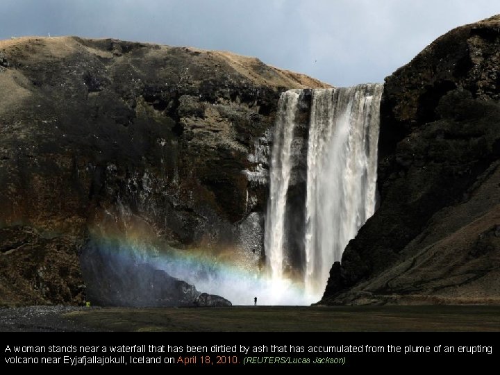 A woman stands near a waterfall that has been dirtied by ash that has