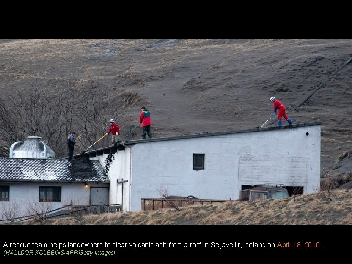 A rescue team helps landowners to clear volcanic ash from a roof in Seljavellir,