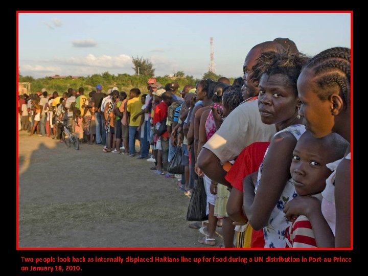 Two people look back as internally displaced Haitians line up for food during a