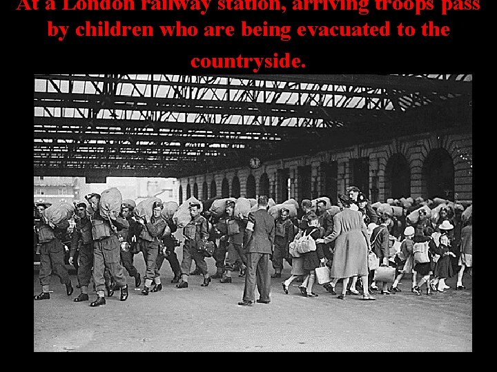 At a London railway station, arriving troops pass by children who are being evacuated