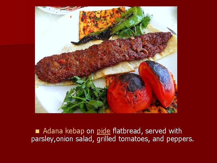 Adana kebap on pide flatbread, served with parsley, onion salad, grilled tomatoes, and peppers.