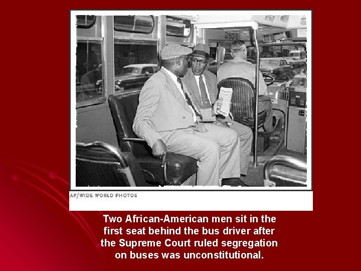 Two African-American men sit in the first seat behind the bus driver after the