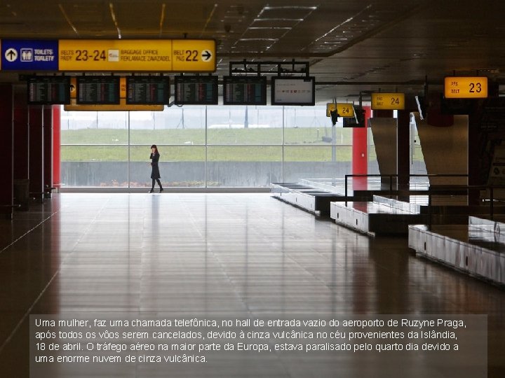 Uma mulher, faz uma chamada telefônica, no hall de entrada vazio do aeroporto de